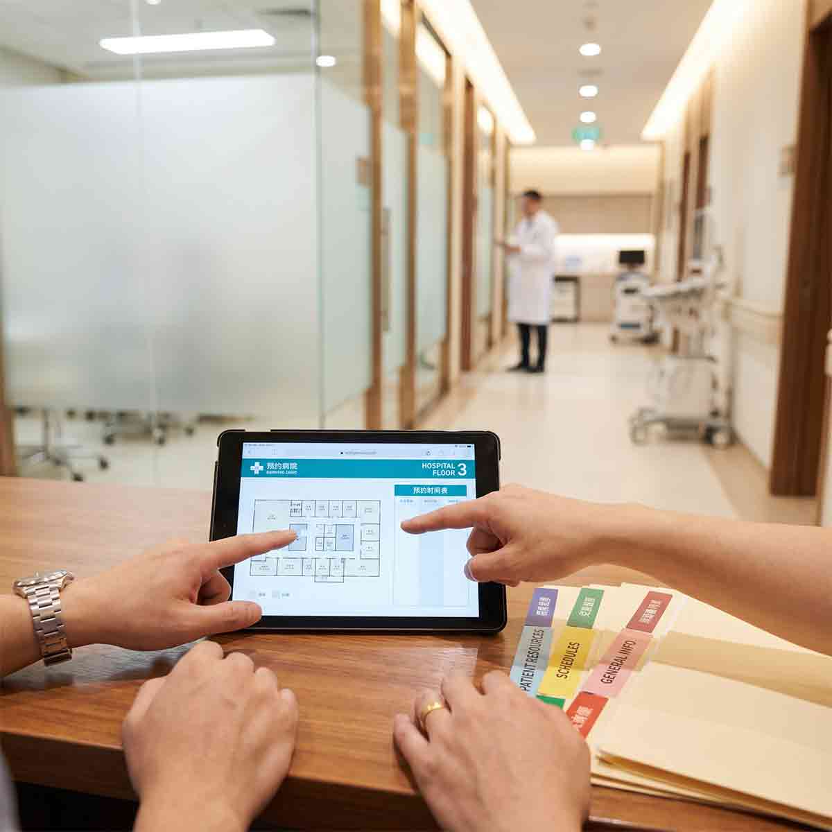 A bilingual coordinator using a tablet to explain hospital navigation and schedules to a client in a modern Chinese medical facility.
